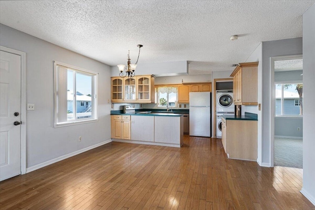 kitchen with freestanding refrigerator, hardwood / wood-style flooring, dark countertops, stacked washer / dryer, and a chandelier