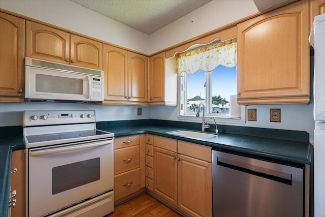 kitchen featuring a textured ceiling, white appliances, dark countertops, and a sink