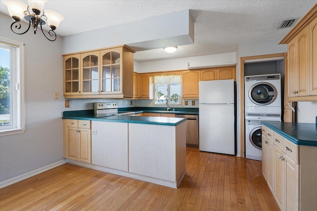 kitchen with visible vents, dark countertops, stacked washing maching and dryer, white appliances, and glass insert cabinets