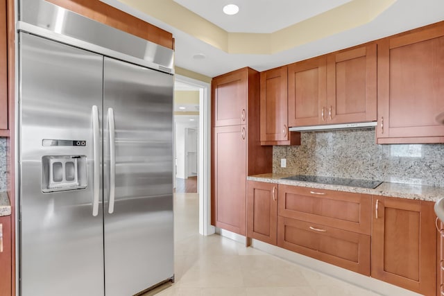 3620 Gardens Pkwy Unit 1001B, Palm Beach Gardens, FL 33410 - kitchen featuring stainless steel built in fridge, black electric stovetop, brown cabinets, under cabinet range hood, and decorative backsplash