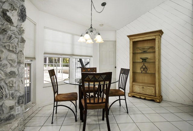 dining space with a notable chandelier, wood walls, and light tile patterned flooring