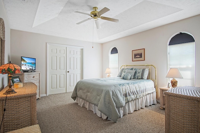 bedroom with a textured ceiling, carpet, a tray ceiling, and a ceiling fan