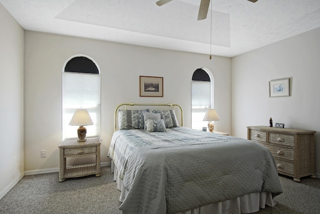 carpeted bedroom with a tray ceiling, baseboards, a textured ceiling, and a ceiling fan