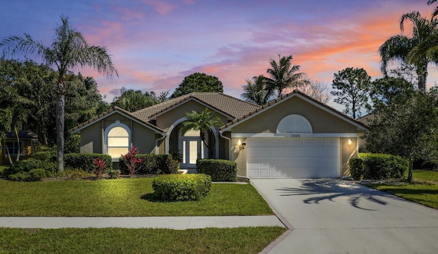 ranch-style house featuring stucco siding, driveway, a front lawn, a tile roof, and a garage