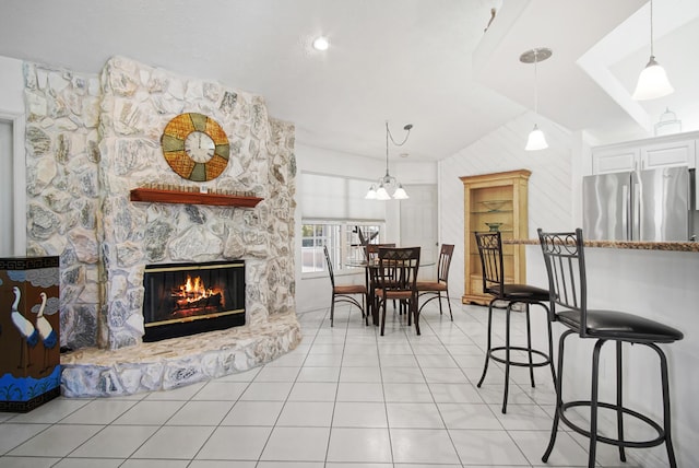 dining room with light tile patterned flooring, a fireplace, and vaulted ceiling