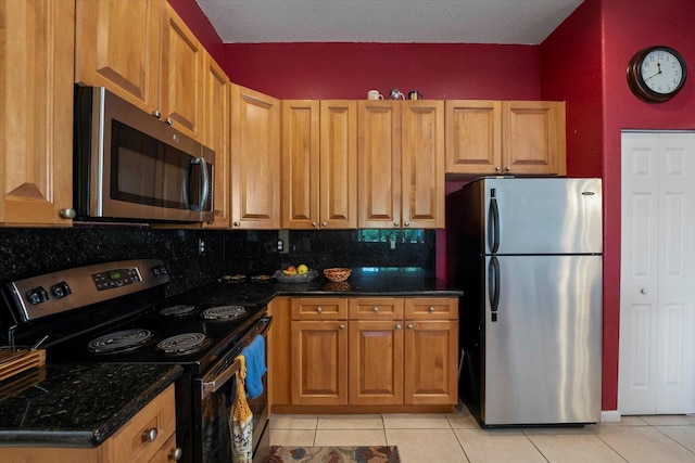 kitchen featuring backsplash, light tile patterned floors, brown cabinets, appliances with stainless steel finishes, and dark stone countertops