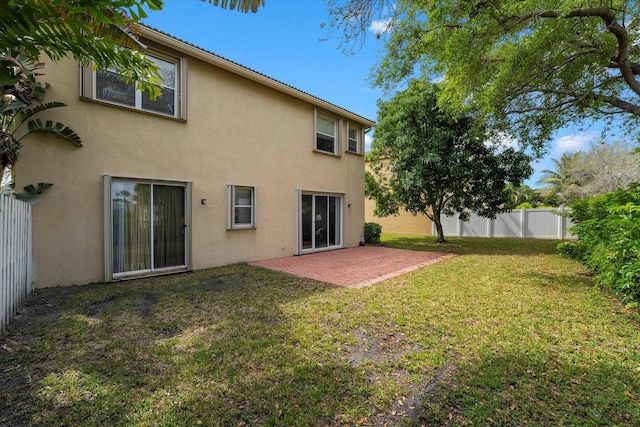 rear view of property with a patio area, stucco siding, a lawn, and fence