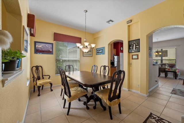 dining area with light tile patterned floors, visible vents, baseboards, an inviting chandelier, and arched walkways