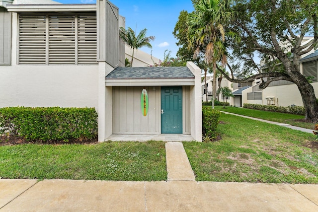 property entrance with a lawn, roof with shingles, and stucco siding