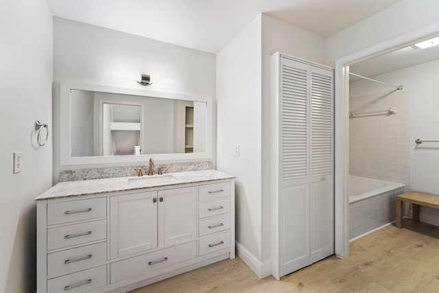 bathroom featuring wood finished floors, a closet, baseboards, bathing tub / shower combination, and vanity