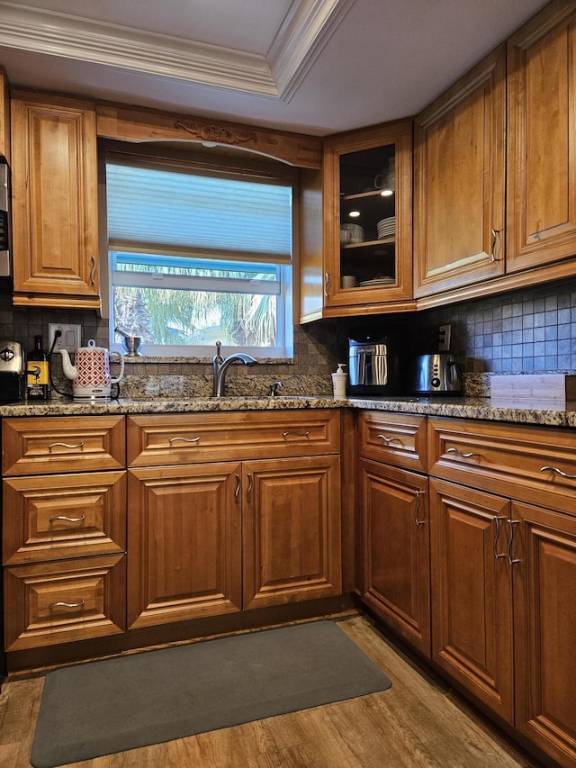 kitchen featuring backsplash, crown molding, stone counters, brown cabinets, and light wood-style floors