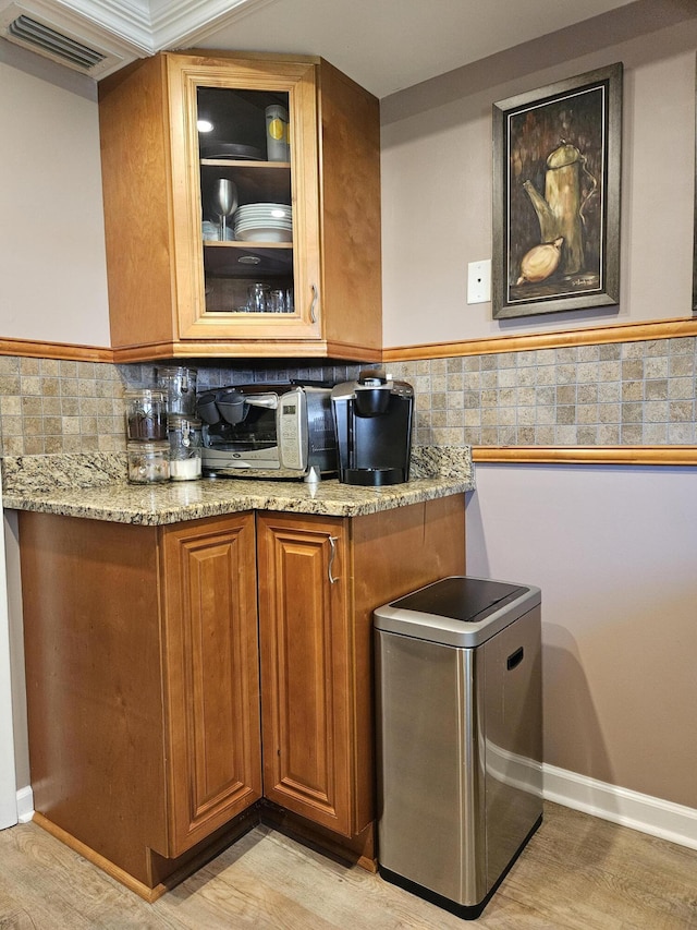 kitchen with light stone counters, visible vents, glass insert cabinets, and brown cabinetry