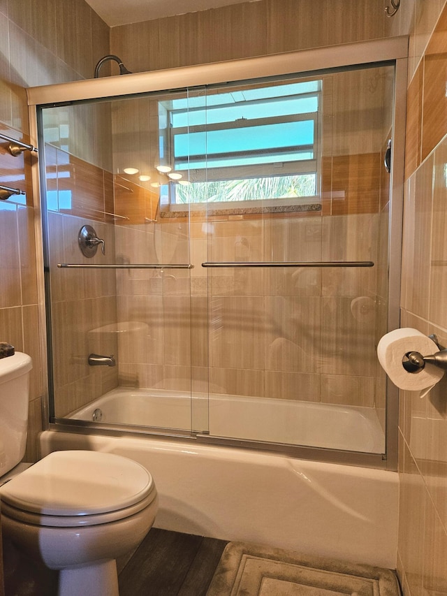 full bath featuring toilet and bath / shower combo with glass door