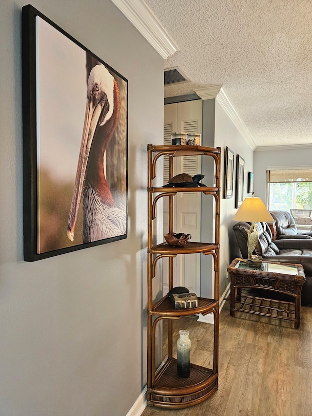 hallway with a textured ceiling, crown molding, baseboards, and wood finished floors