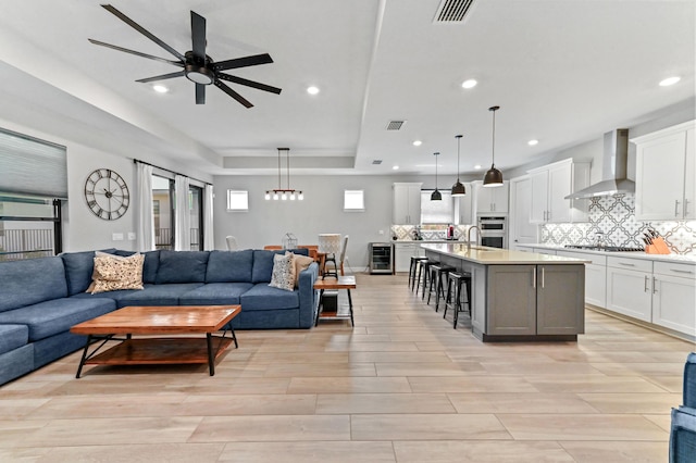 living room featuring a tray ceiling, wine cooler, ceiling fan, and visible vents