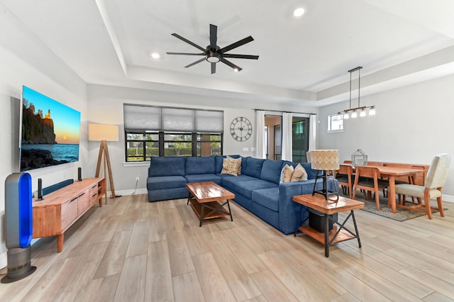 living area featuring a tray ceiling, baseboards, and light wood-type flooring