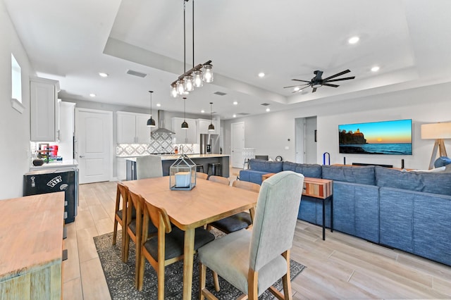 dining room with a ceiling fan, a raised ceiling, wood tiled floor, and visible vents