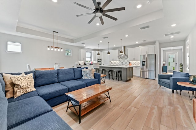 living room with a tray ceiling, a healthy amount of sunlight, light wood-type flooring, and a ceiling fan
