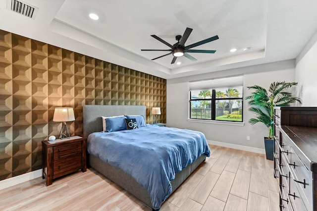bedroom with visible vents, baseboards, light wood-type flooring, a tray ceiling, and an accent wall