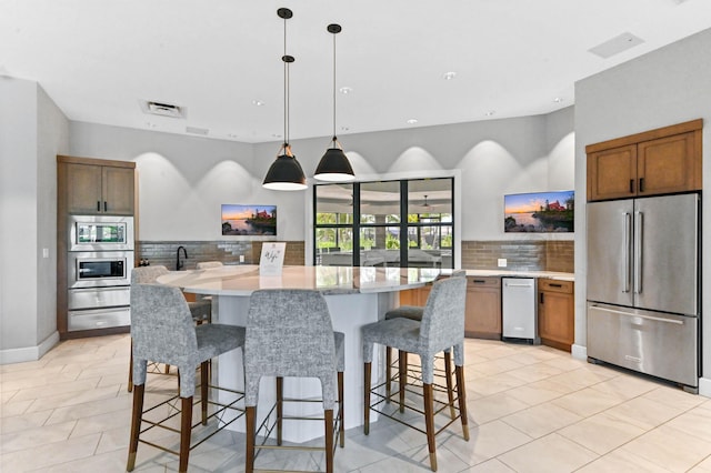 kitchen with a breakfast bar, decorative backsplash, pendant lighting, visible vents, and appliances with stainless steel finishes