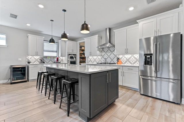 kitchen featuring light countertops, wine cooler, wall chimney range hood, light wood-style flooring, and appliances with stainless steel finishes