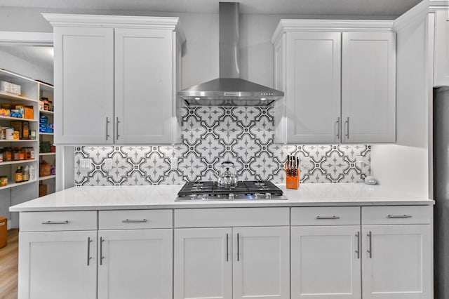 kitchen with stainless steel gas stovetop, light countertops, white cabinets, wall chimney exhaust hood, and tasteful backsplash