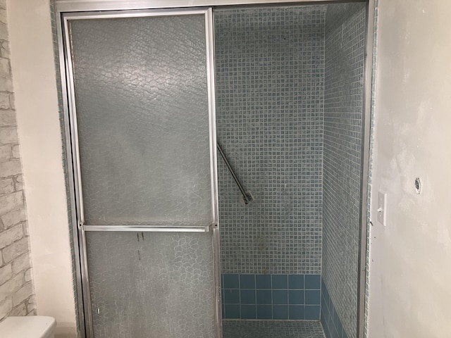 full bathroom featuring a stall shower, toilet, and a textured wall