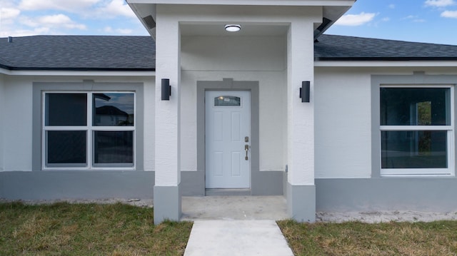 entrance to property featuring roof with shingles and stucco siding