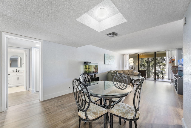 dining space featuring visible vents, a textured ceiling, wood finished floors, a skylight, and baseboards