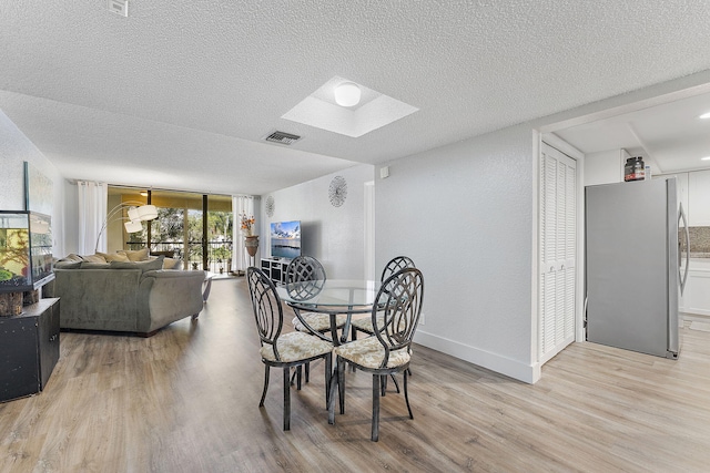 dining room featuring light wood-style flooring, a skylight, baseboards, and a textured ceiling