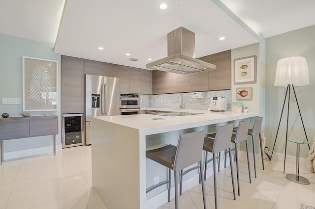 kitchen featuring modern cabinets, island exhaust hood, wine cooler, appliances with stainless steel finishes, and a peninsula