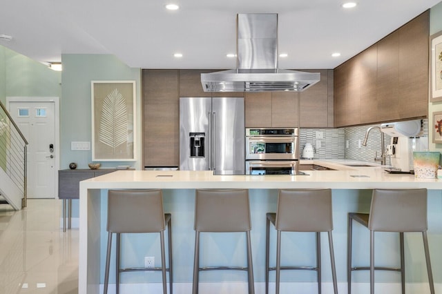 kitchen with light countertops, appliances with stainless steel finishes, island range hood, modern cabinets, and a sink