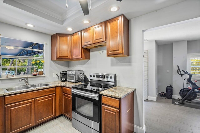 kitchen with ornamental molding, light stone counters, stainless steel electric range, a raised ceiling, and a sink