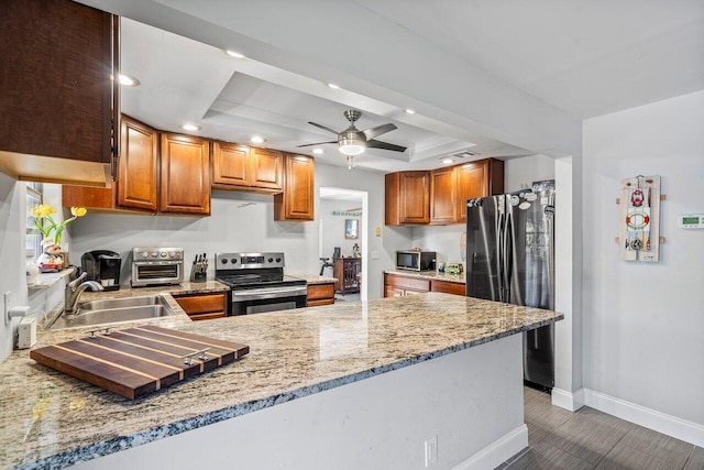 kitchen with light stone countertops, a toaster, a tray ceiling, stainless steel appliances, and a sink