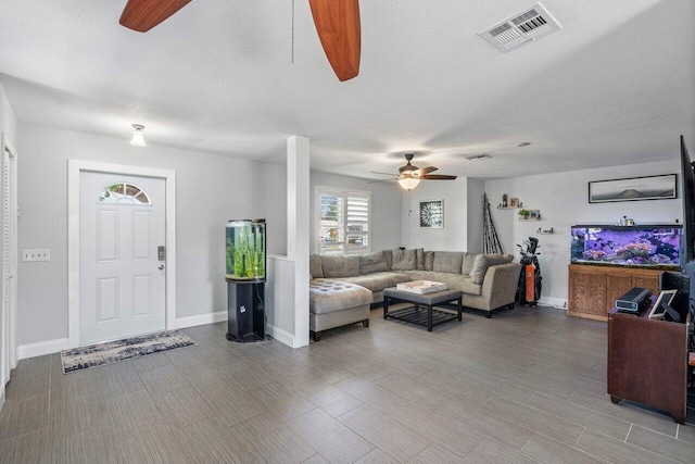 living room featuring visible vents, baseboards, a textured ceiling, and a ceiling fan