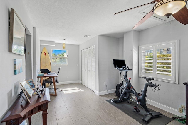 workout area featuring visible vents, a ceiling fan, baseboards, and a textured ceiling