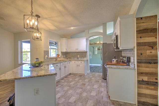 kitchen featuring a chandelier, lofted ceiling, a peninsula, white cabinets, and a sink
