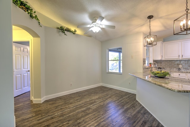 unfurnished dining area featuring baseboards, ceiling fan with notable chandelier, arched walkways, dark wood-style floors, and a textured ceiling