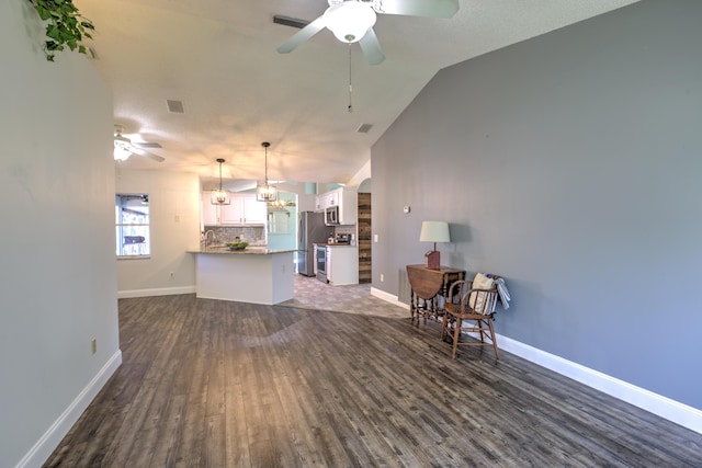 living area featuring dark wood finished floors, lofted ceiling, ceiling fan with notable chandelier, and baseboards