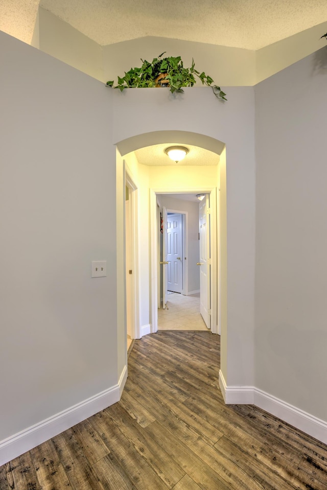 corridor with arched walkways, a textured ceiling, baseboards, and wood finished floors