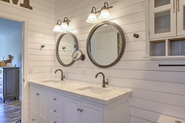 bathroom with double vanity, wooden walls, wood finished floors, and a sink