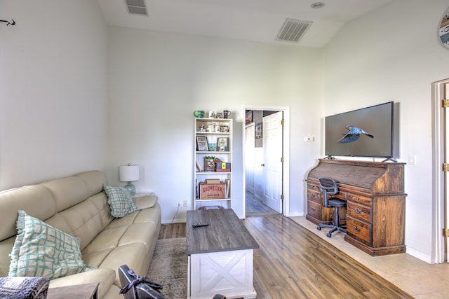 living room featuring vaulted ceiling, visible vents, baseboards, and wood finished floors