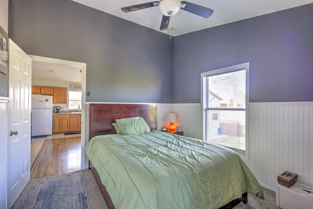 bedroom with a wainscoted wall, a ceiling fan, a sink, freestanding refrigerator, and light wood finished floors