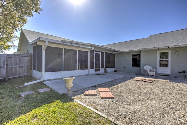 back of house with stucco siding, fence, roof with shingles, a sunroom, and a patio area