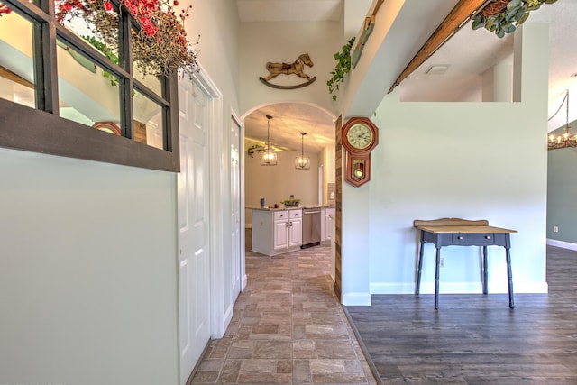 hall with baseboards, a high ceiling, arched walkways, stone finish flooring, and a chandelier