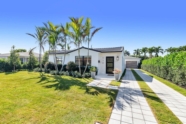 view of front of home with a detached garage, a front lawn, and stucco siding