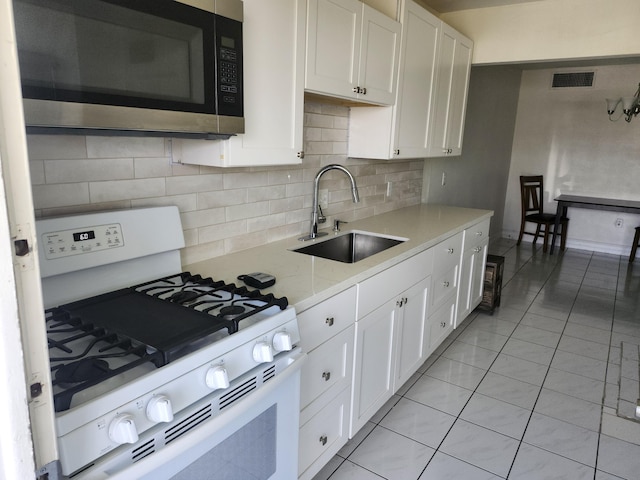 kitchen with white gas stove, a sink, decorative backsplash, white cabinetry, and stainless steel microwave