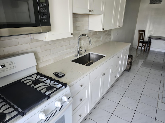 kitchen featuring stainless steel microwave, light stone counters, white range with gas cooktop, white cabinets, and a sink