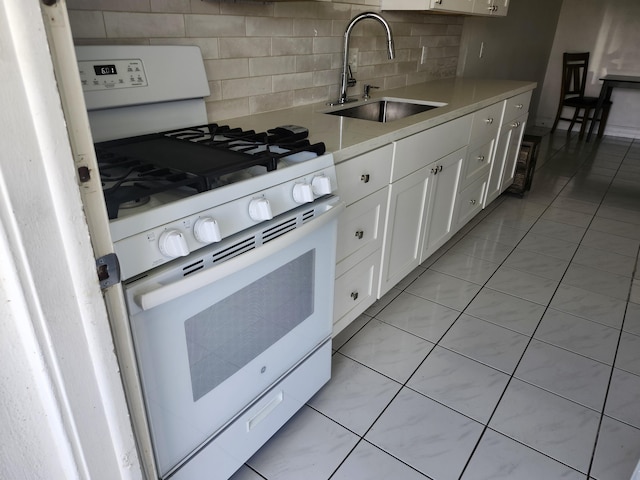 kitchen with tasteful backsplash, light countertops, white gas range, white cabinets, and a sink