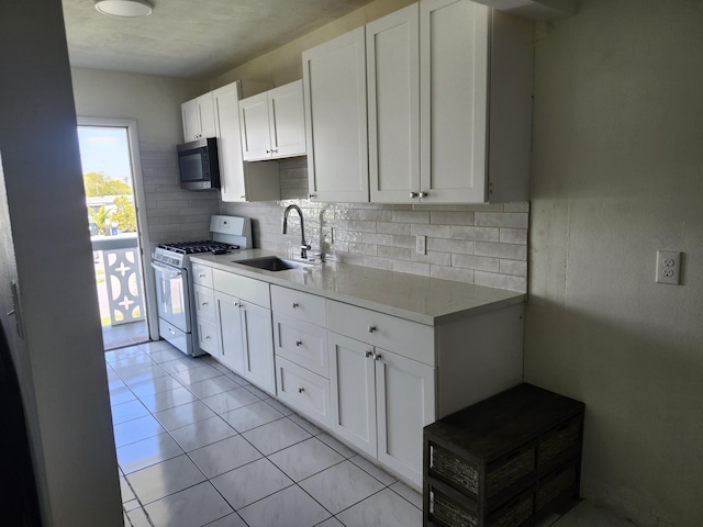 kitchen featuring stainless steel microwave, white gas stove, decorative backsplash, white cabinetry, and a sink